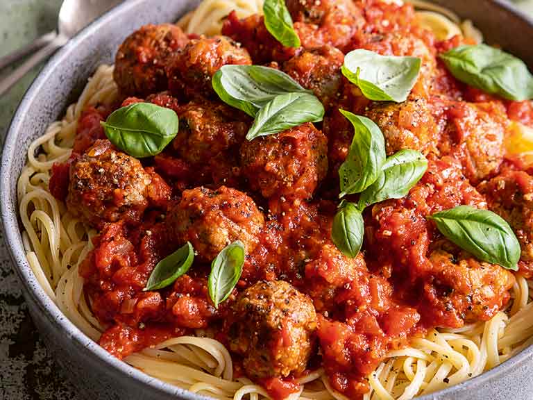 Dish of spaghetti covered in tomato sauce with meatballs and garnished with basil leaves