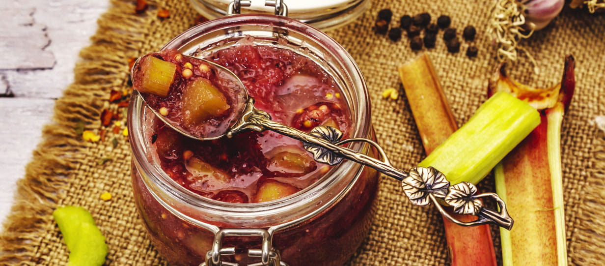 An open mason jar filled with rhubarb chutney with a decorative spoon lying across the top