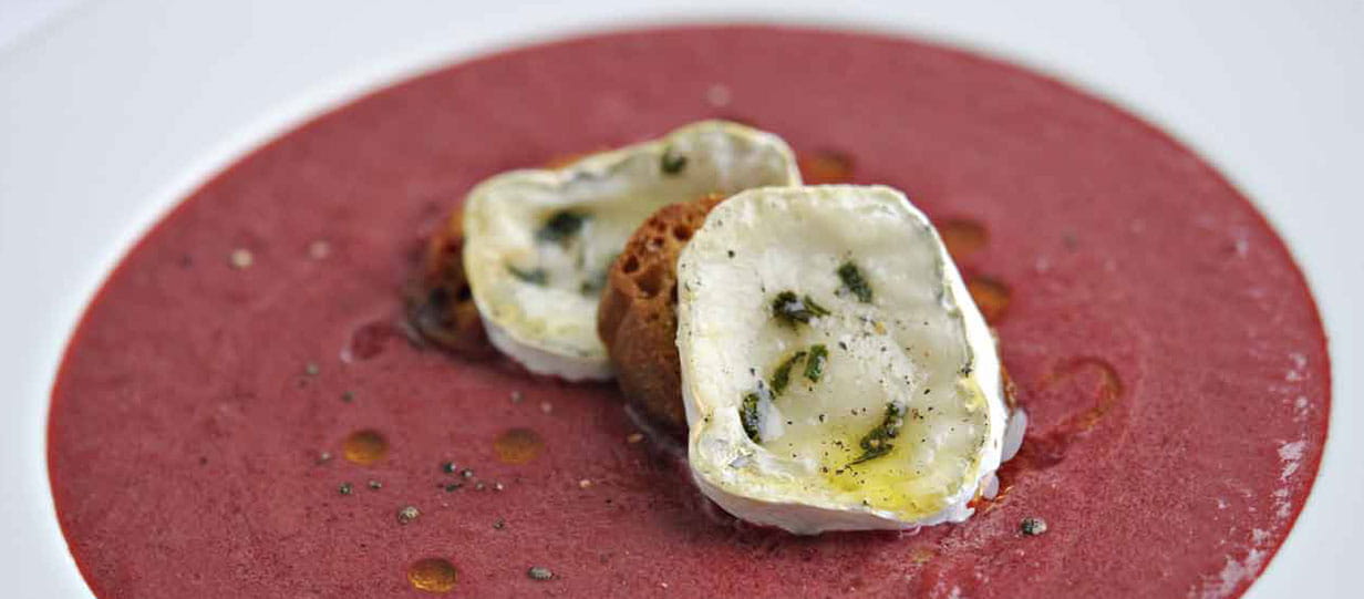 Bowl of beetroot soup topped with croutons and goats cheese