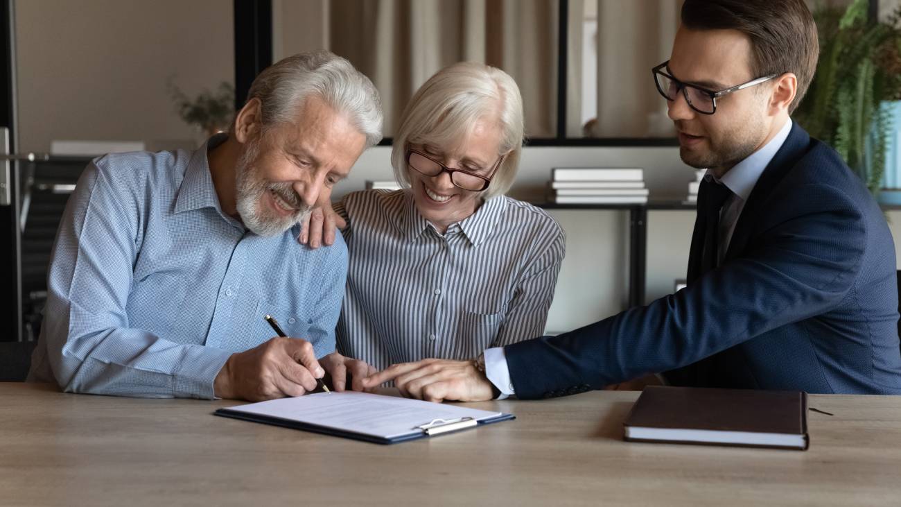 Mature couple sitting at a table with a lawyer signing a contract 