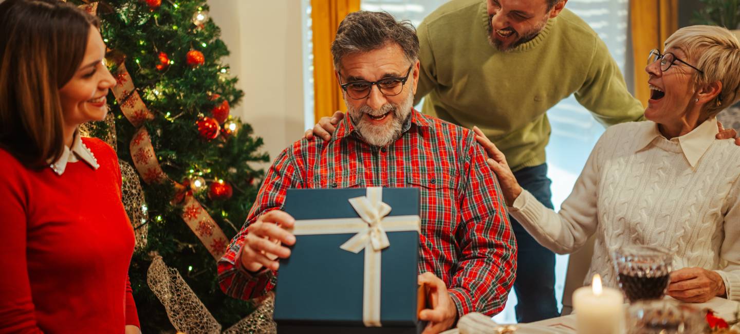 Family is gathered around a festive table enjoying their christmas dinner and giving a present to their father and grandfather