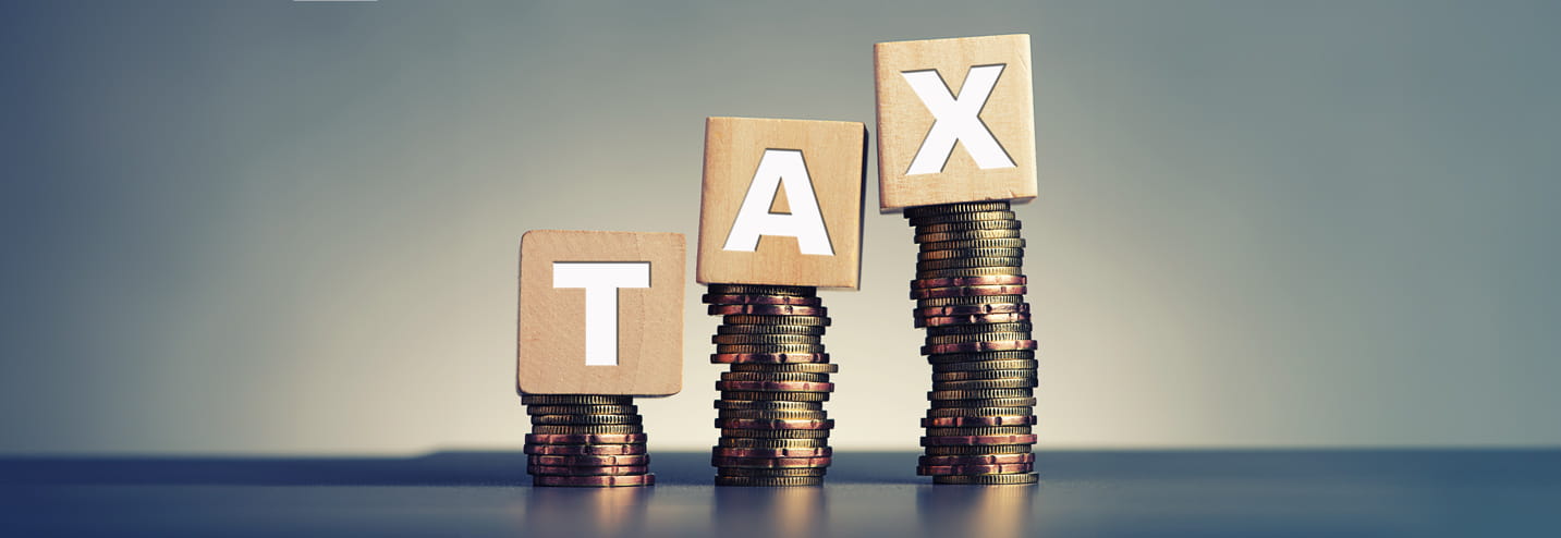 3 piles of coins with wooden blocks on top spelling out the word tax