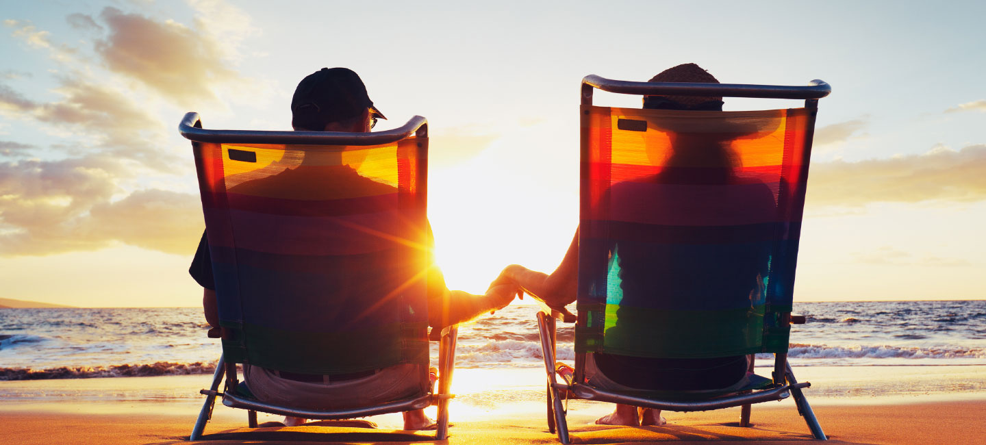 Two people sitting in deckchairs holding hands looking at the sunset