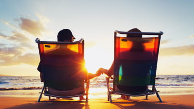 A couple in deckchairs holding hands looking at the sunset