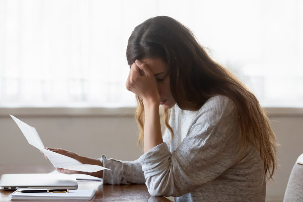A woman holding paperwork with her head in her hand