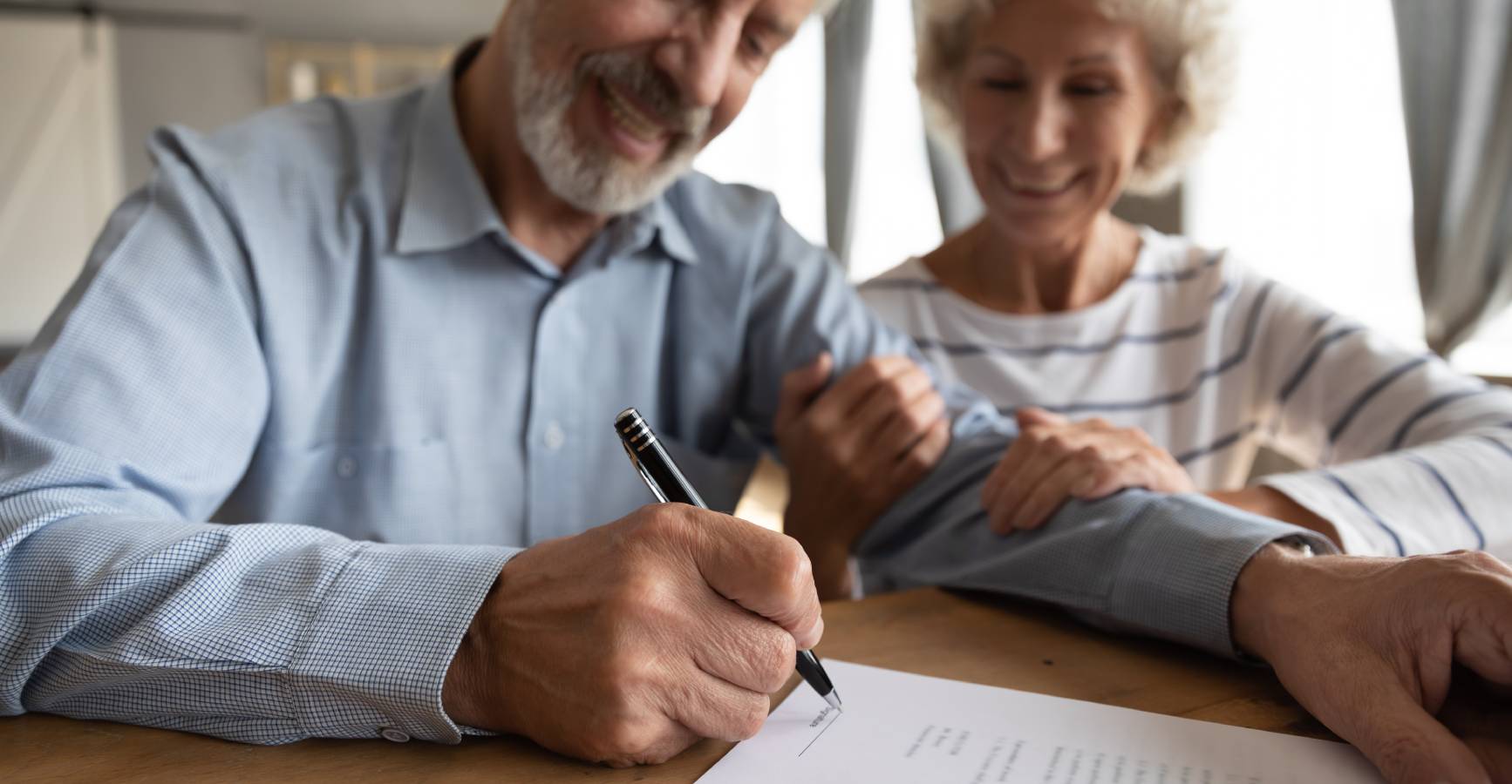 Close up satisfied older couple signing documents, making purchasing or investment deal, smiling mature husband and wife holding hands, putting signature on contract, buying house or taking loan