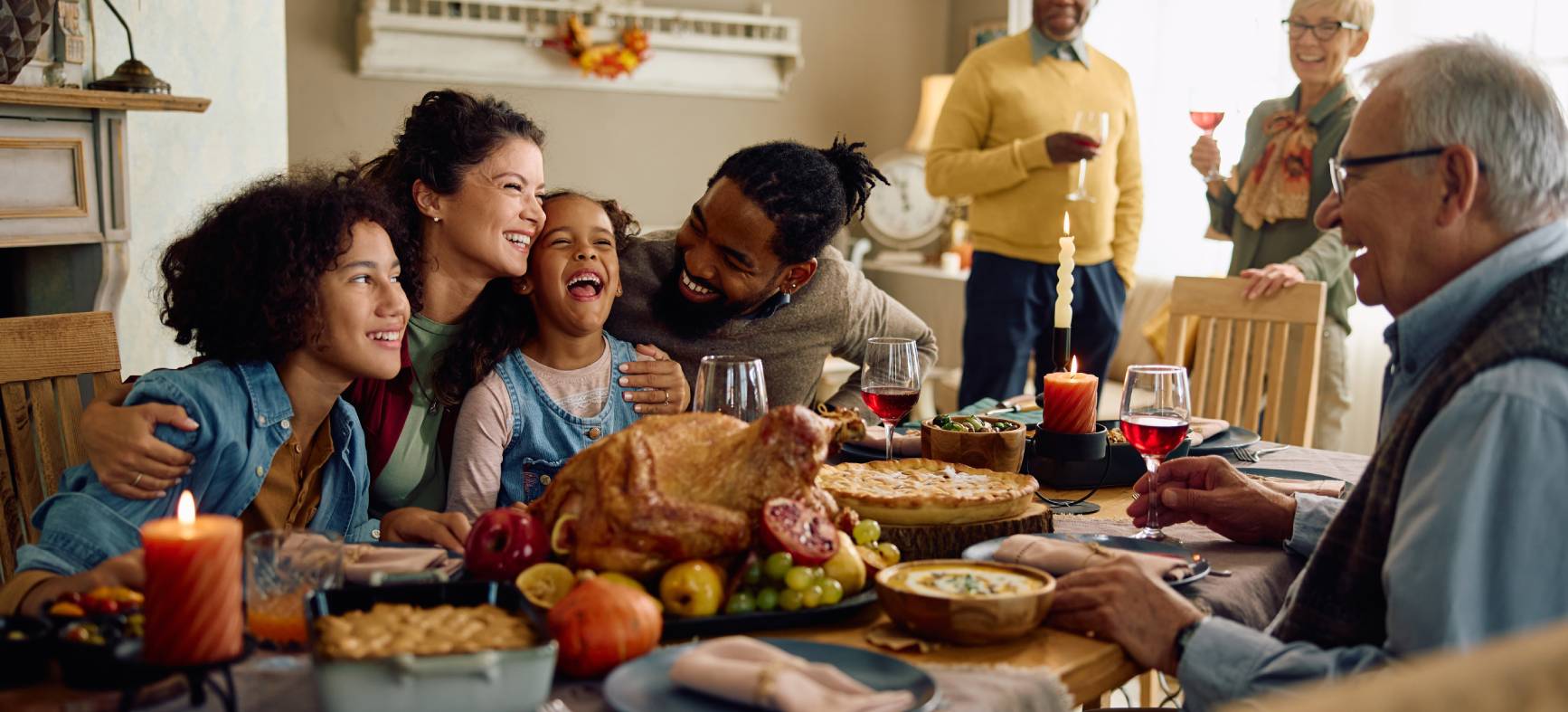 Happy multiracial parents and their kids laughing during family meal on Thanksgiving in dining room. 