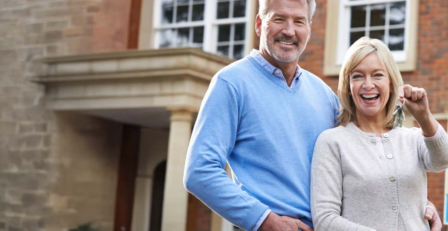 A couple stood outside their home holding a set of keys out to the camera