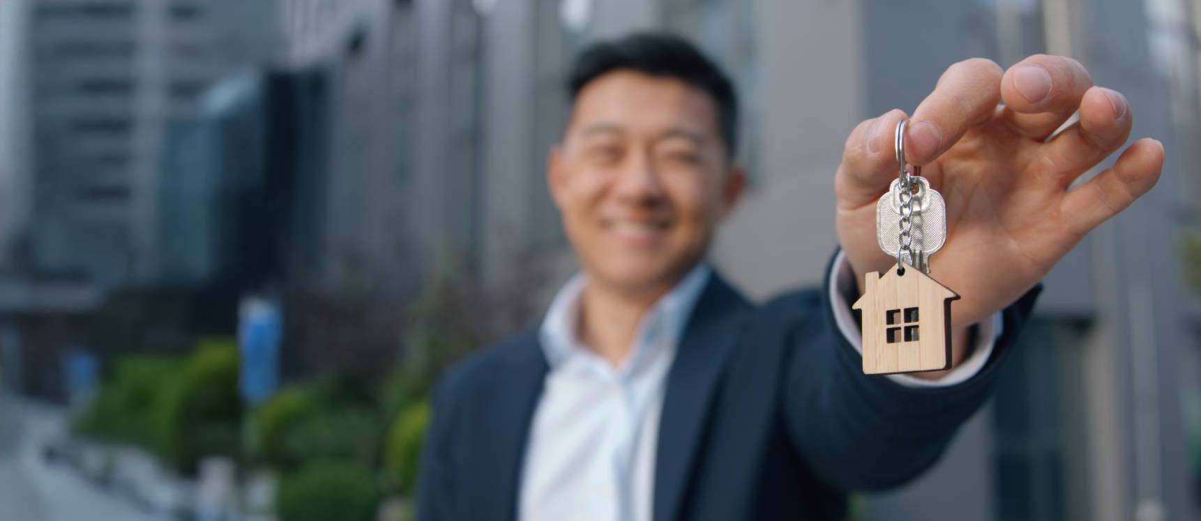 A man holding out a keyring with a wooden house on it