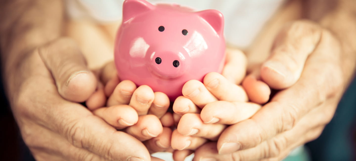 Adult hands cupping a child's hands holding a piggy bank