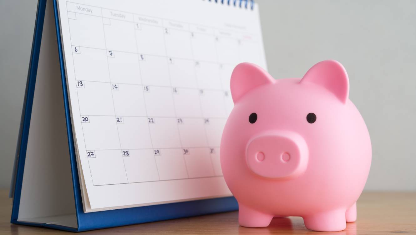 Pink piggy bank and white blank calendar on white background. Reminder schedule of savings money, DCA (dollar cost averaging) investment, money management planning concept. Home finance and economy.