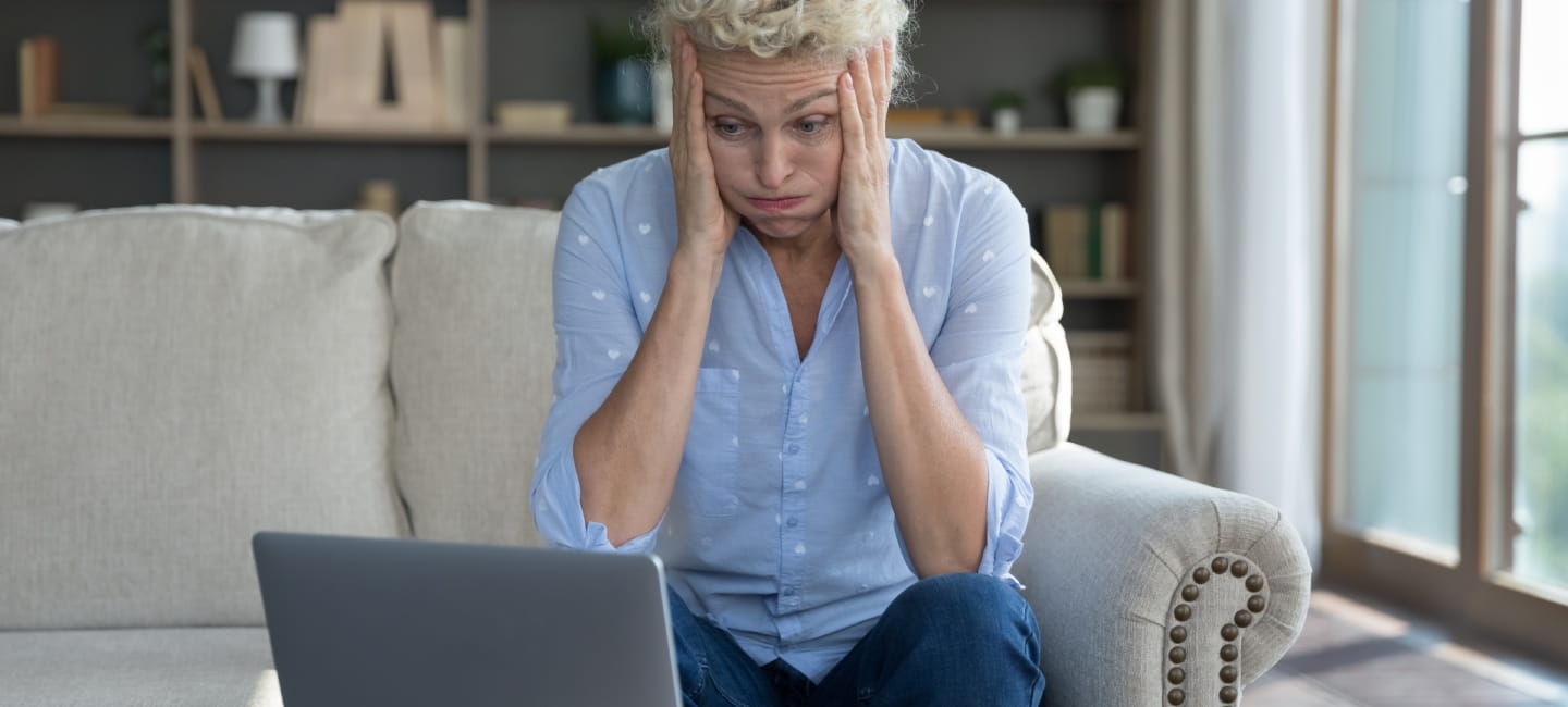A distressed woman looking at her laptop with her head in her hands
