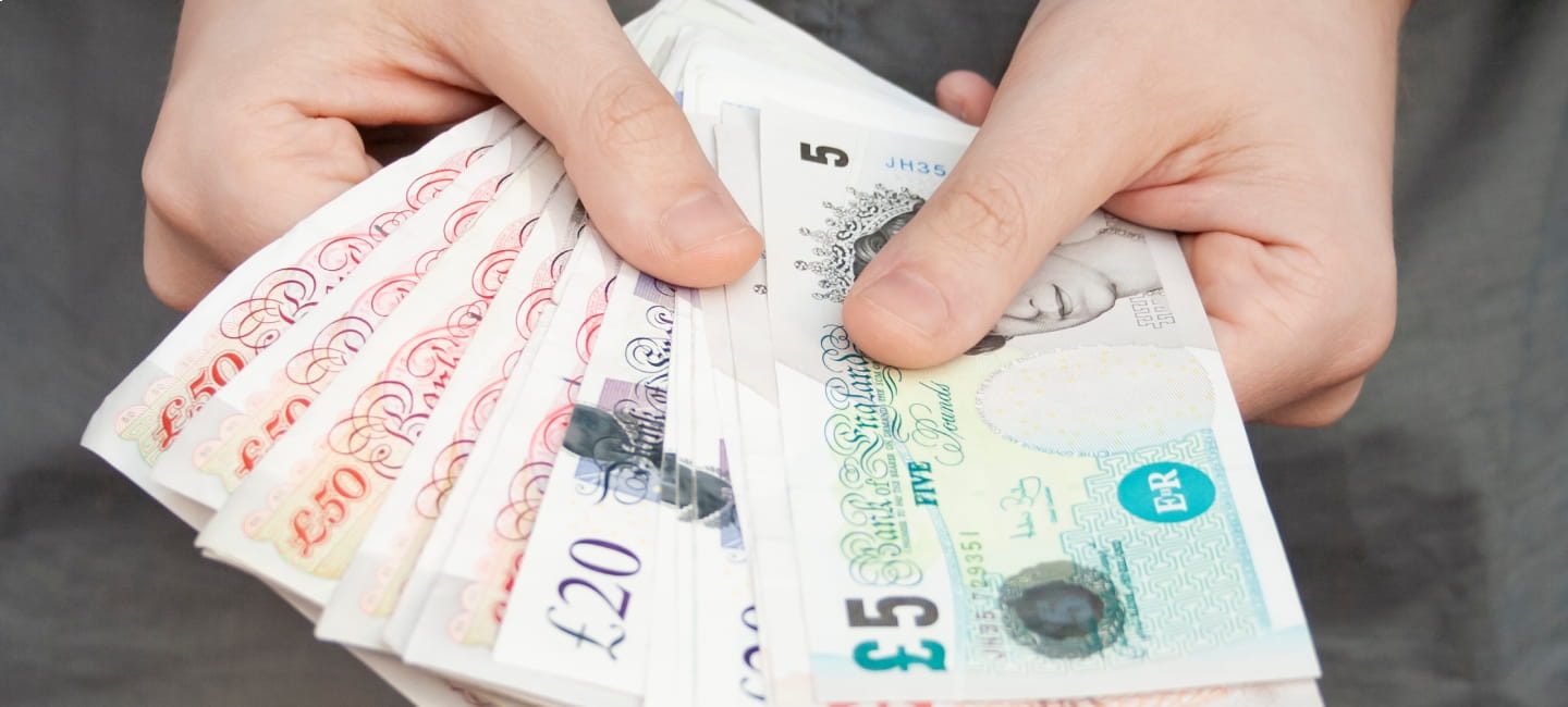 A person holding several £5, £10 and £20 notes