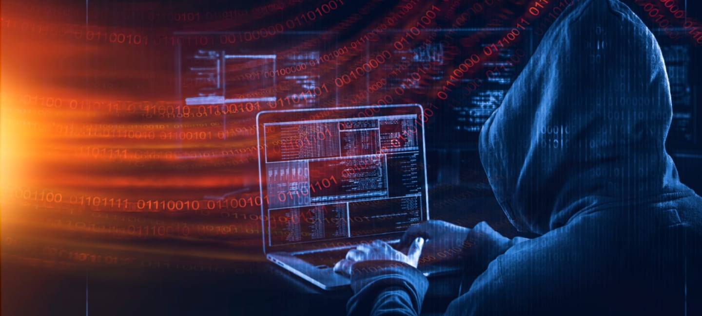 A shadowy figure typing at a laptop 