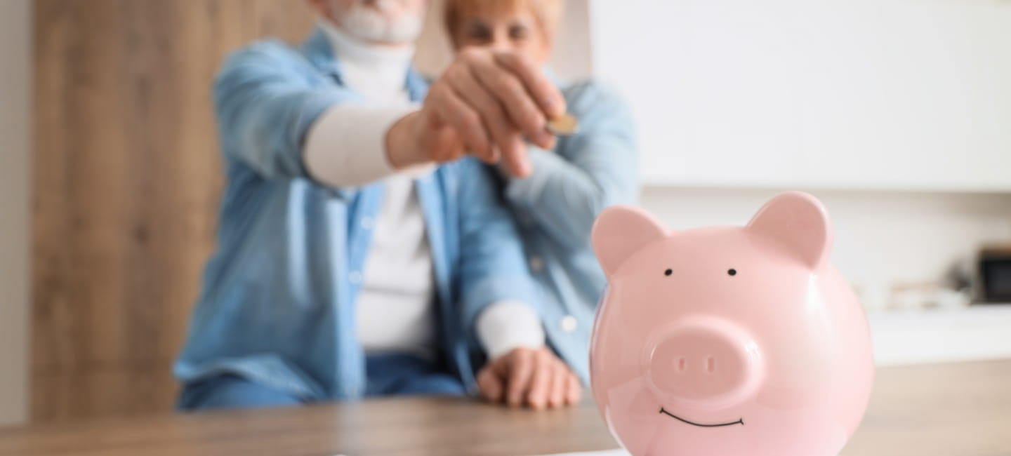 Mature couple putting coin into piggy bank in kitchen, closeup