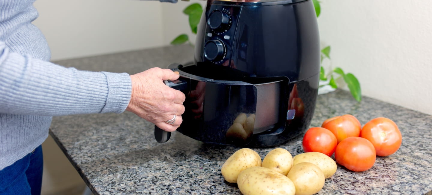 Using airfryer to fry food in home kitchen, with tomatoes and potatoes nearby