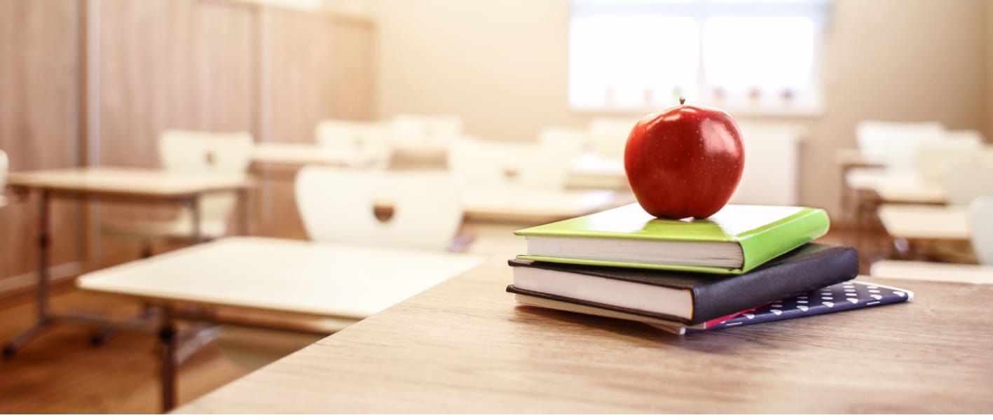 School teacher's desk with stack of books and apple