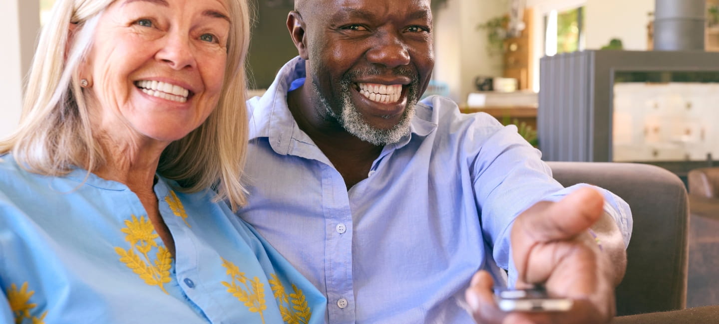 Multi-Racial Senior Couple On Sofa At Home Together Watching TV.