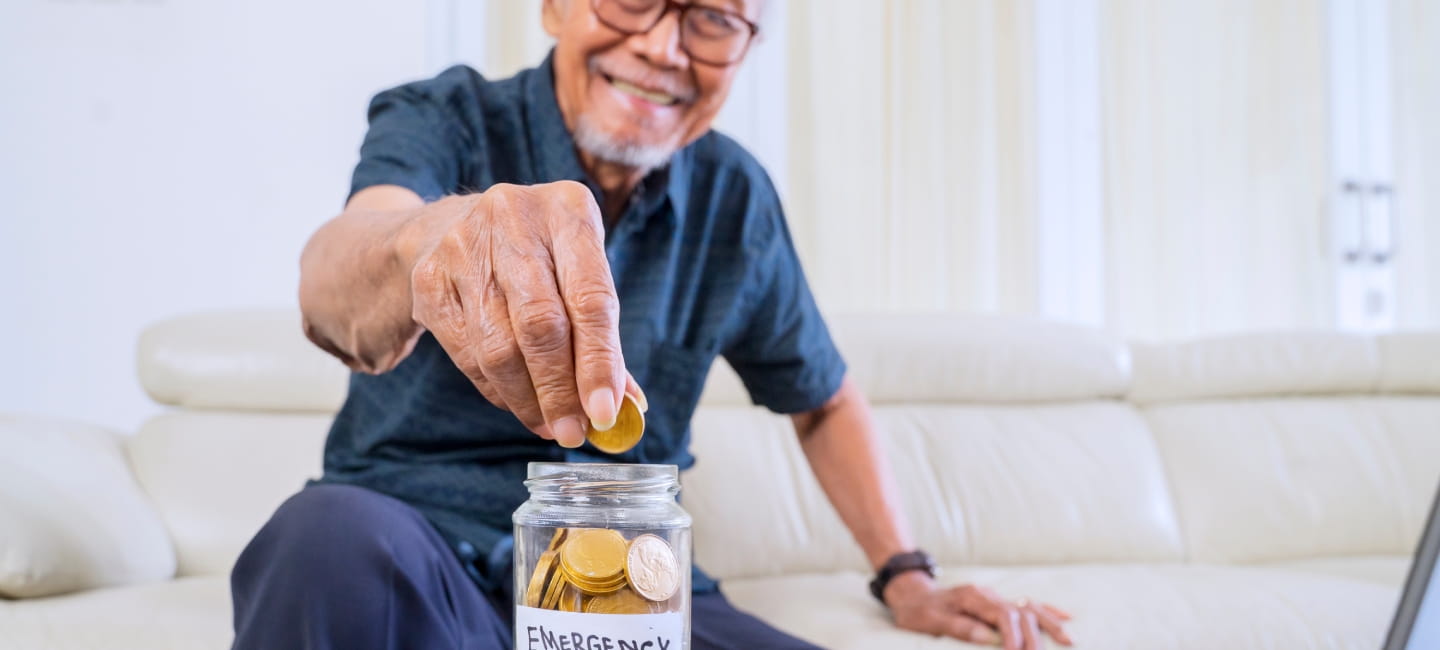 Happy senior man savings golden coins in a jar with retirement text and laptop on the table