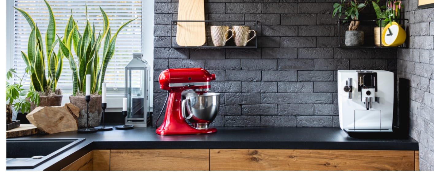 Wooden clock on black brick wall in trendy kitchen with red kitchen robot.