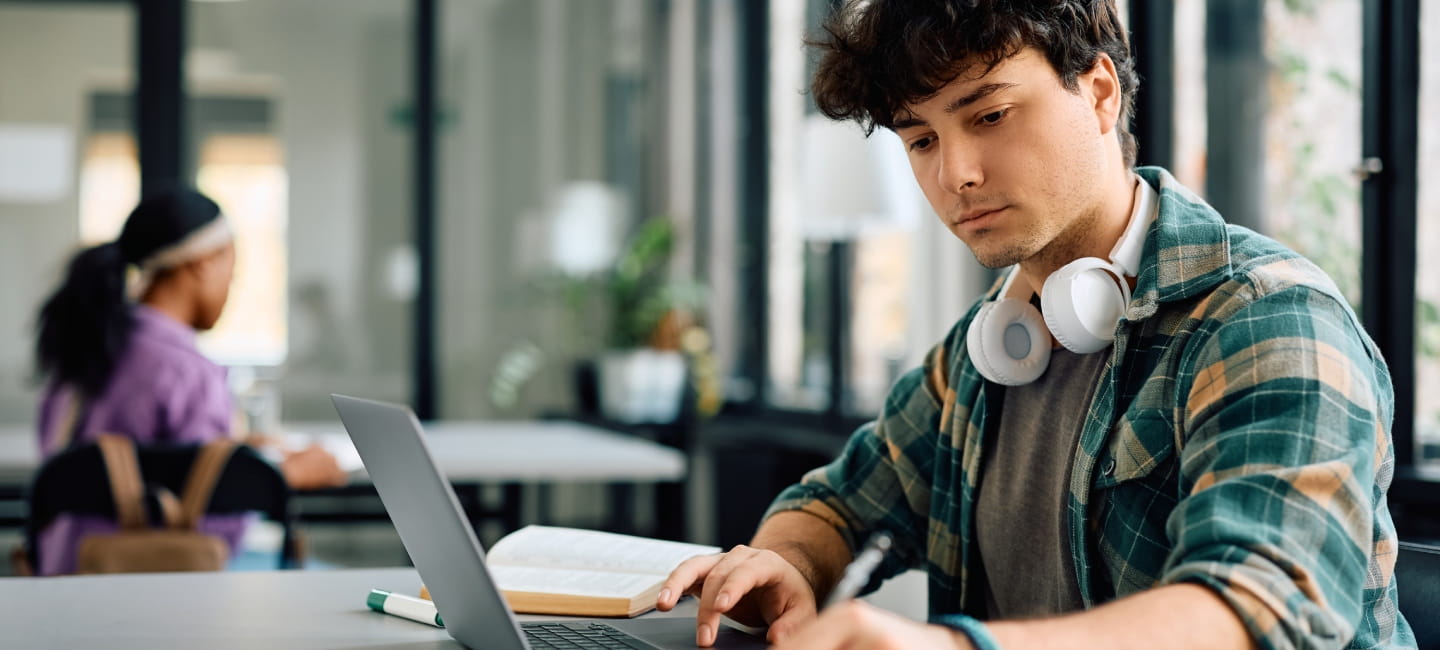 University student writing while using laptop and studying in the classroom. Copy space.