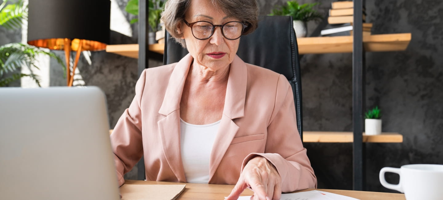 Concentrated caucasian senior businesswoman manager counting funds earnings bills on calculator in office. Serious grandmother paying domestic bills, loan, mortgage, insurance