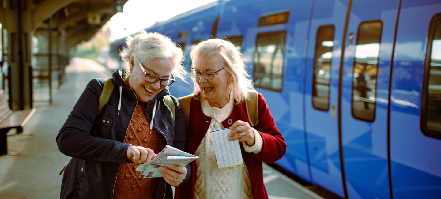 Two senior women at train station with map.