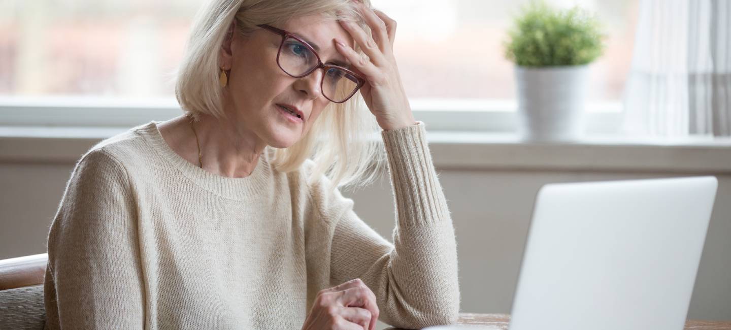 Thoughtful confused mature woman concerned thinking about online problem looking at laptop.