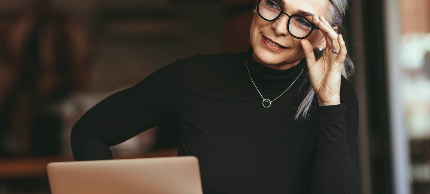 Senior businesswoman sitting at cafe with laptop looking away and thinking.