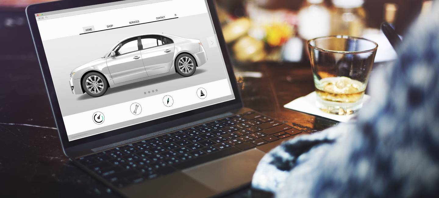 Person sitting at a table with a glass of coke and ice, with a laptop with a car model on it