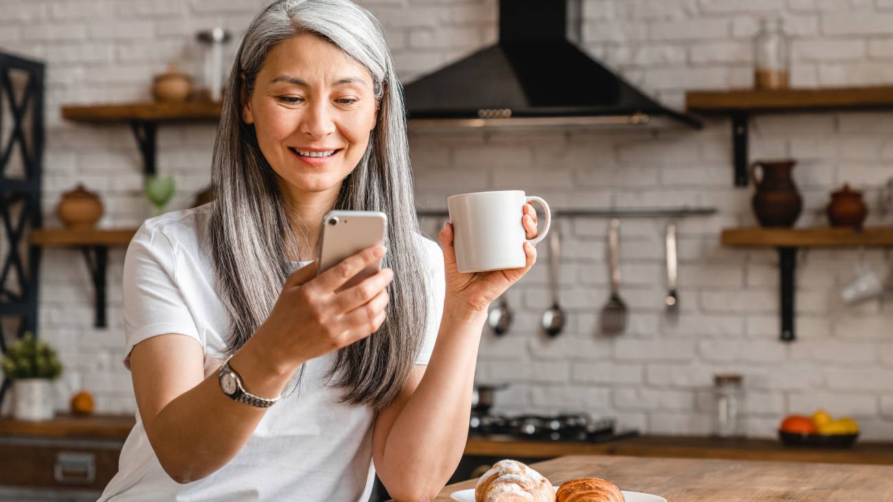 mature woman drinking tea and looking at her phone