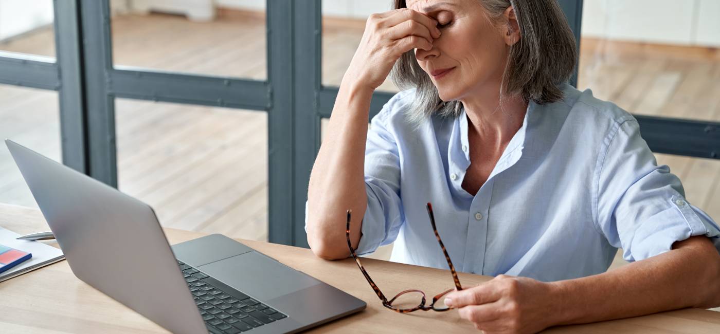 Overworked tired mature lady holding glasses feeling headache, having eyesight problem after computer work. Stressed mature senior business woman rubbing dry eyes at workplace.
