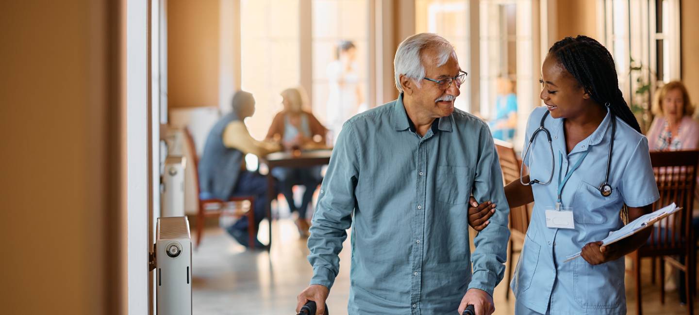Happy senior man using mobility walker while a nurse is helping him in nursing home.