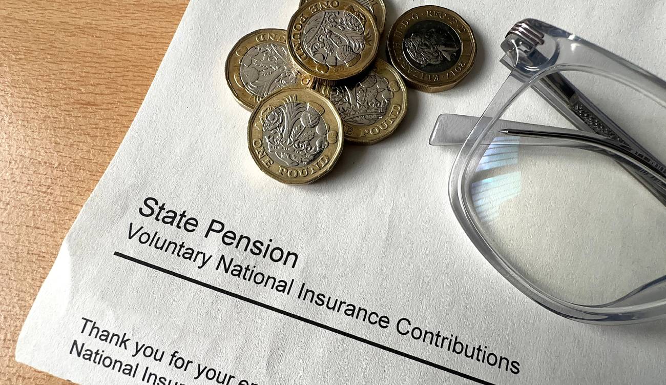 British one pound coins on top of an official letter about paying voluntary national insurance contributions towards the State Pension.