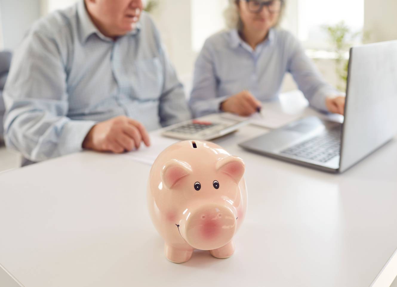 Senior couple sitting at table with piggy bank and calculating finances or taxes at home
