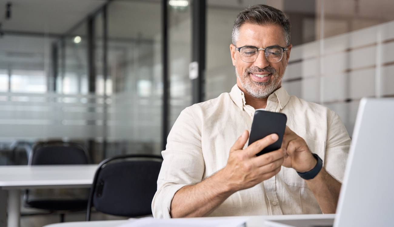 Middle aged Hispanic business manager ceo using cell phone mobile app, laptop.