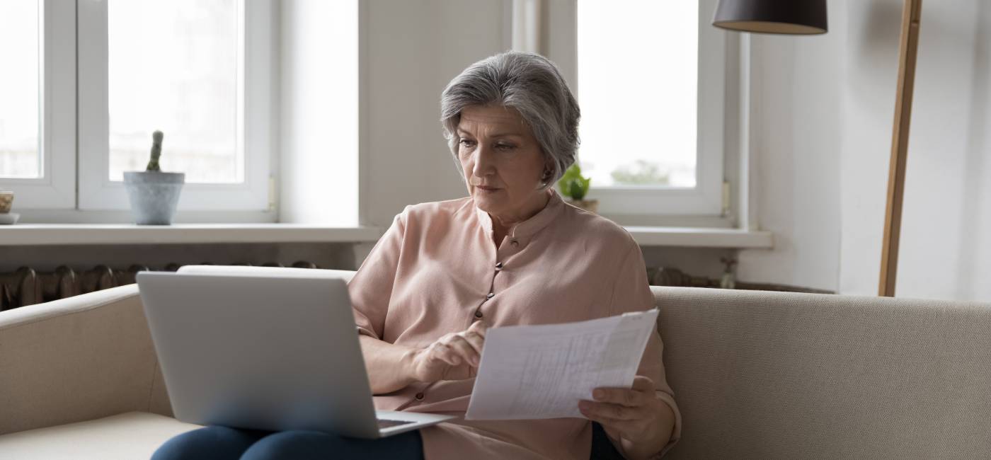 grey-haired woman sits on sofa with laptop looking for national insurance number