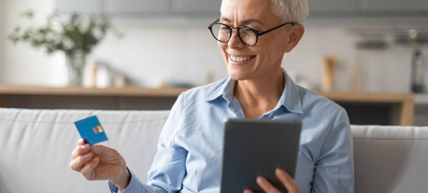 Smiling senior woman shopping online using digital tablet and holding her a blue credit or discount card