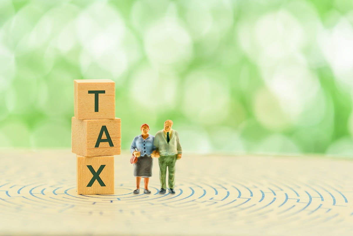 Vertical wooden toy blocks spelling tax with two wooden people stood next to them