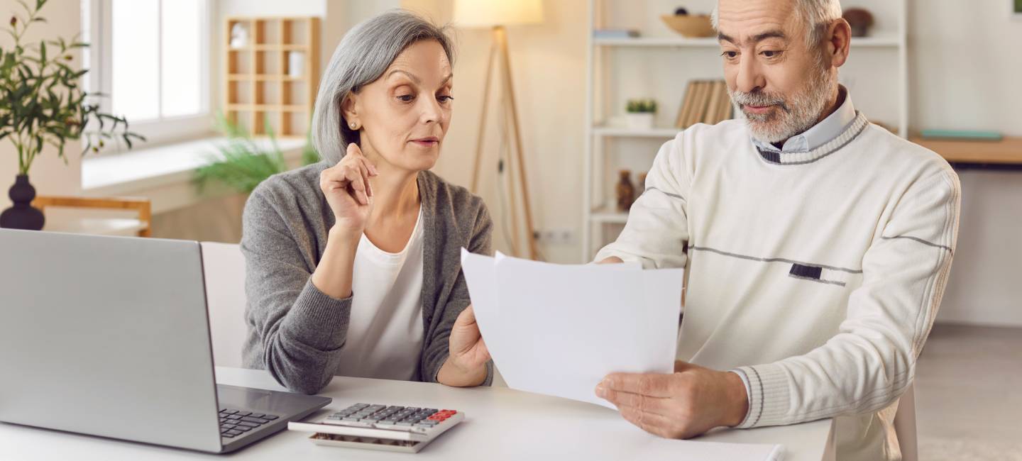 Elderly couple sits and working together at a table in home, reviewing bills