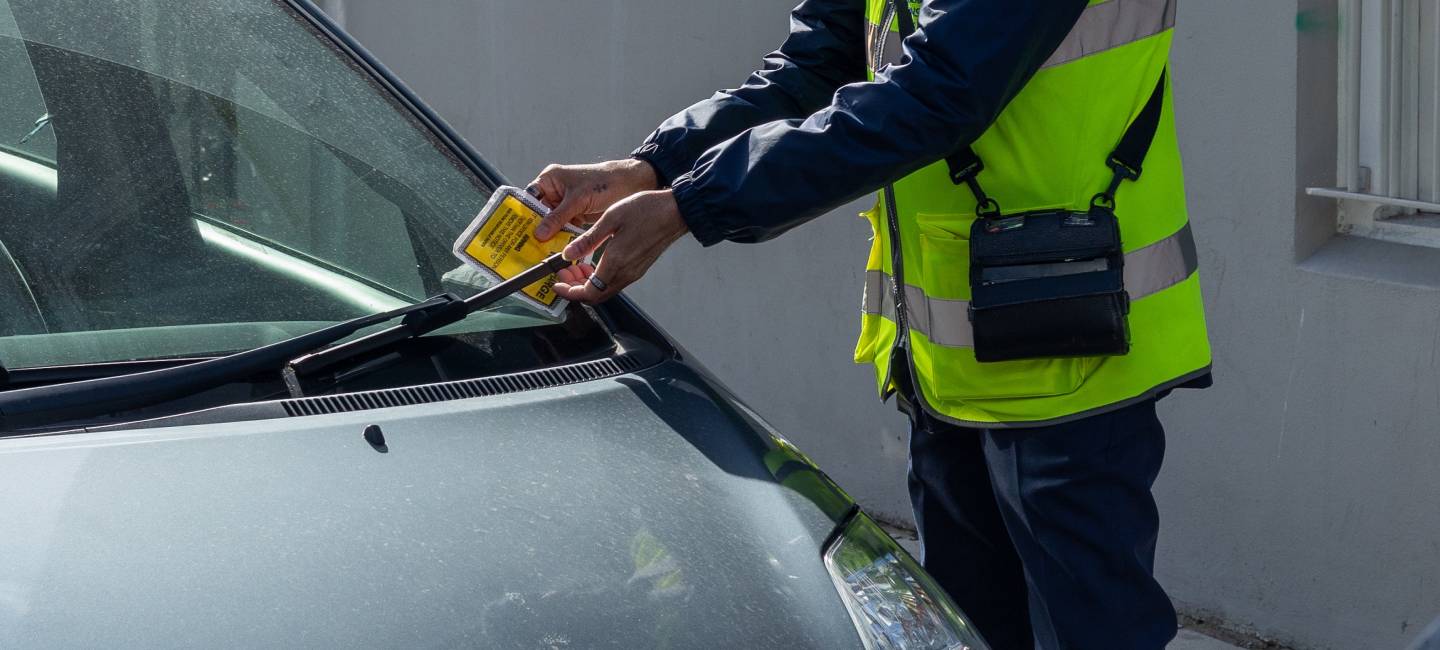 "Traffic warden in the UK puts a parking fine ticket on the window of a car"
