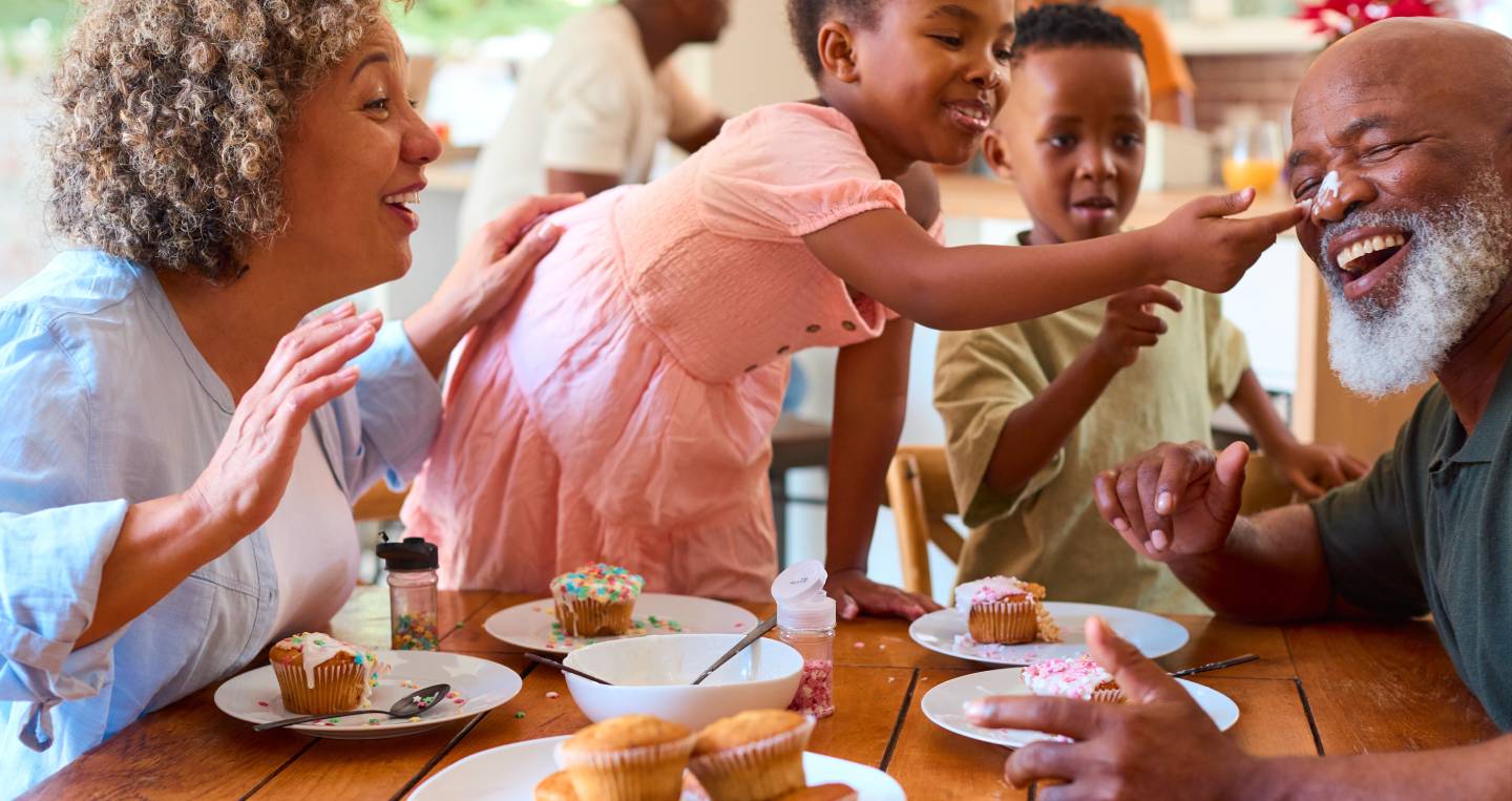 Grandparents With Grandchildren Indoors At Home Decorating Cakes Together With Family In Background