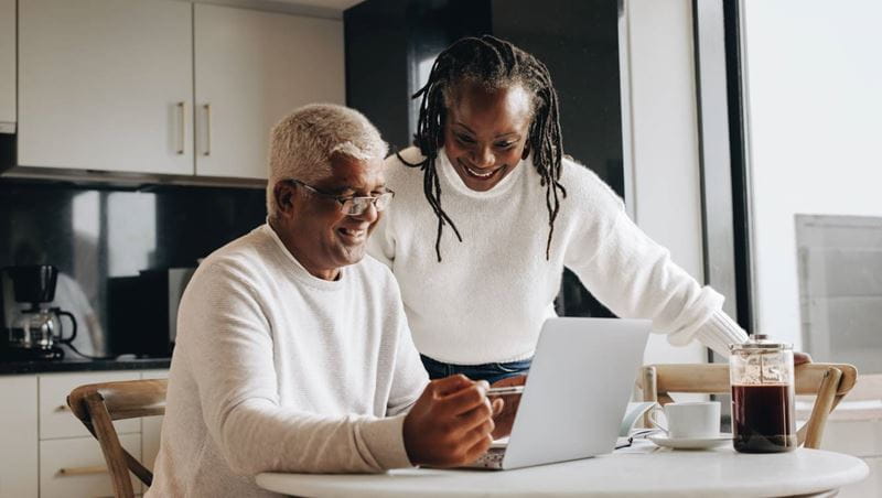 Cheerful senior couple smiling happily while looking at a laptop screen.