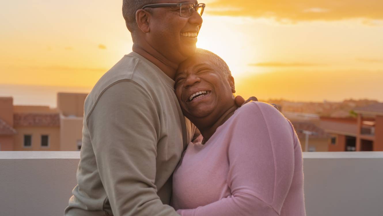 Happy Latin senior couple having romantic moment embracing on rooftop during sunset time - Elderly people love concept 