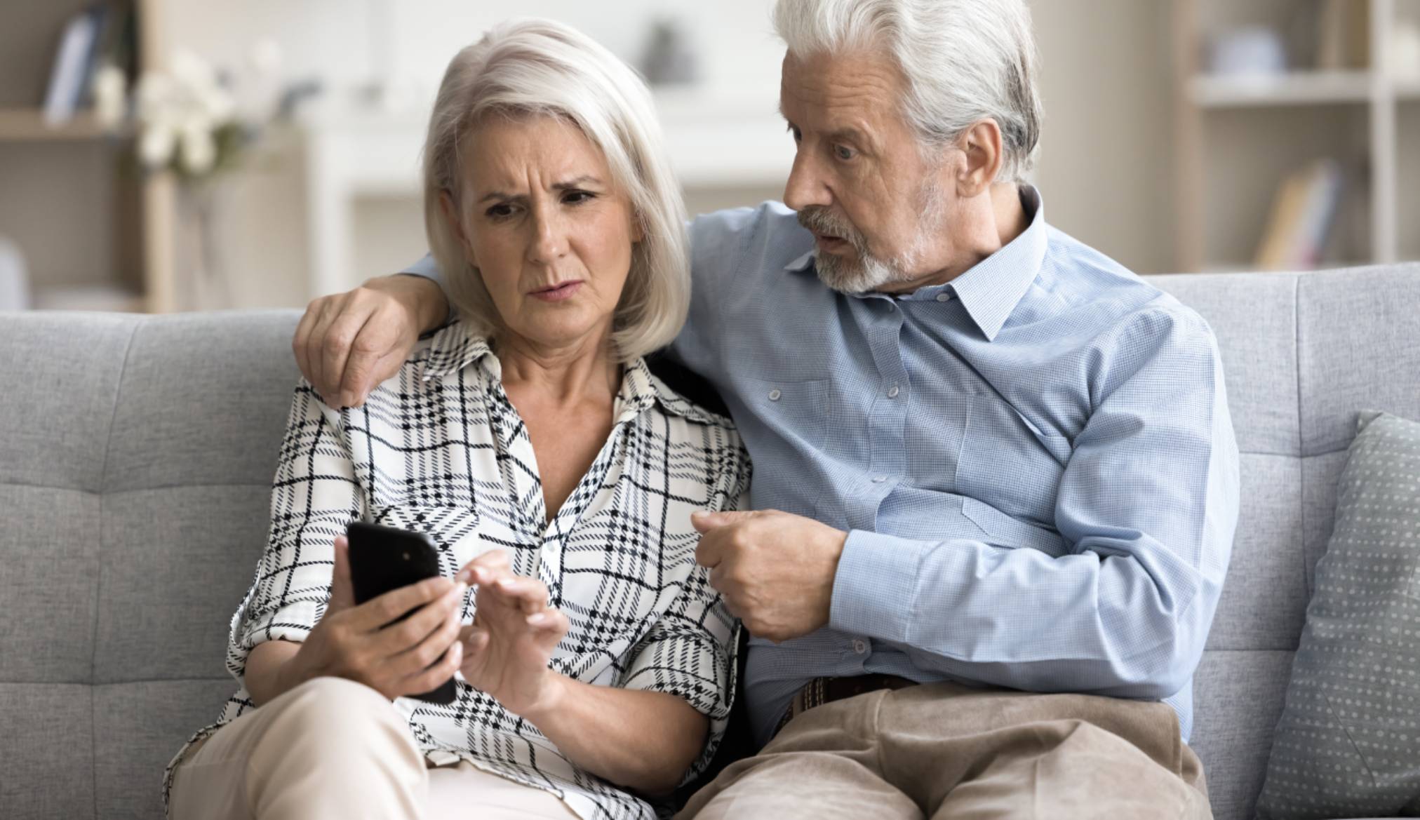 Anxious concerned older couple using mobile phone together. Worried mature wife showing smartphone screen to surprised senior husband, discussing communication problem, trouble