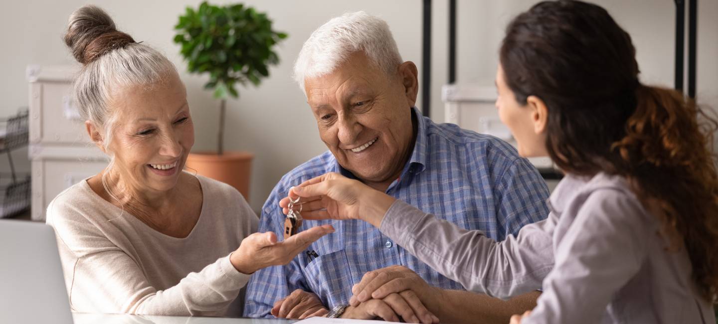 Excited senior husband wife become homeowners receive keys from new home in estate agents office