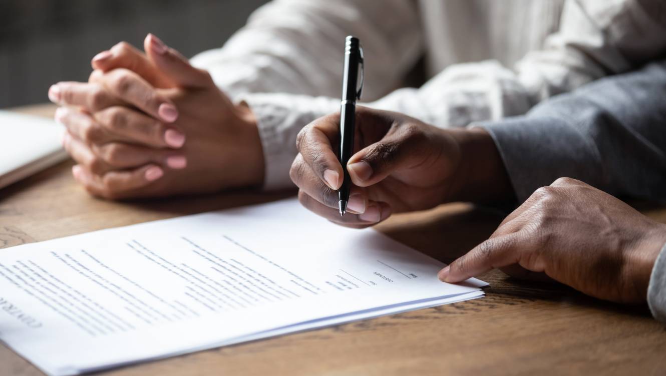 Close up of african American husband put signature on contract buying first house with wife, multiracial couple sign agreement closing deal with realtor or banker, taking property loan or mortgage