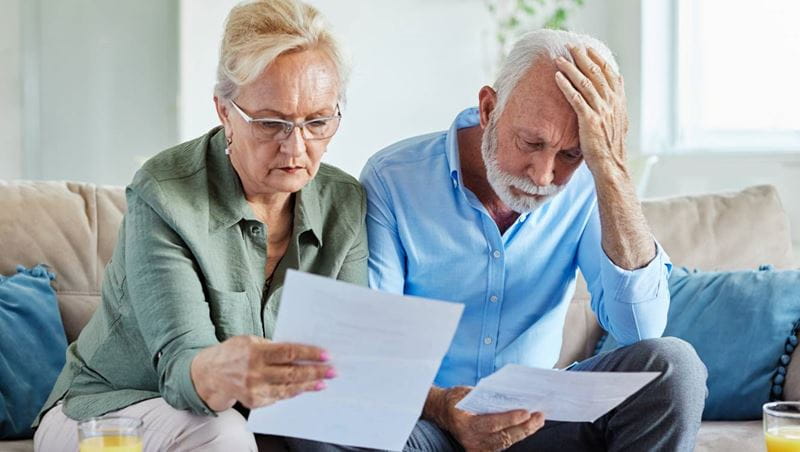 Senior couple checking bills and calculating expenses using a calculator at home, debt taxes and home budget concept, worried married elderly couple