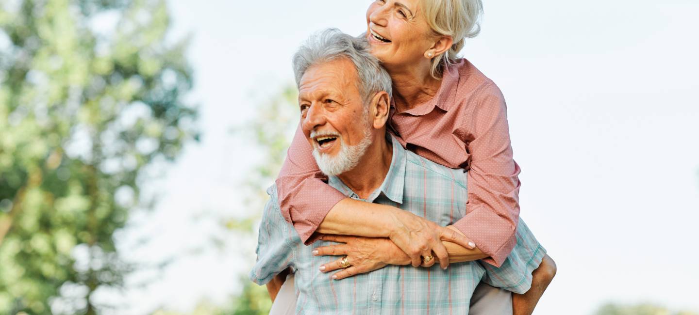 Happy active senior couple having fun outdoors. The man is lifting the woman on his back.