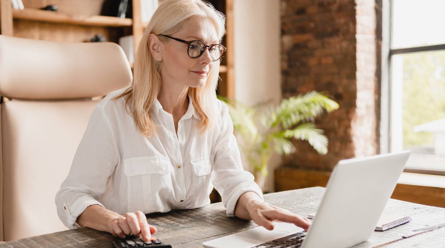 Middle-aged mature businesswoman boss financial advisor counting on calculator funds, money, paying domestic bills, debts, credit loan using laptop in office